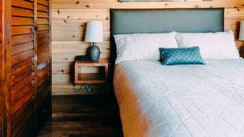 Una habitación de madera con una cama, una mesita de noche y una lámpara fijada a la pared.