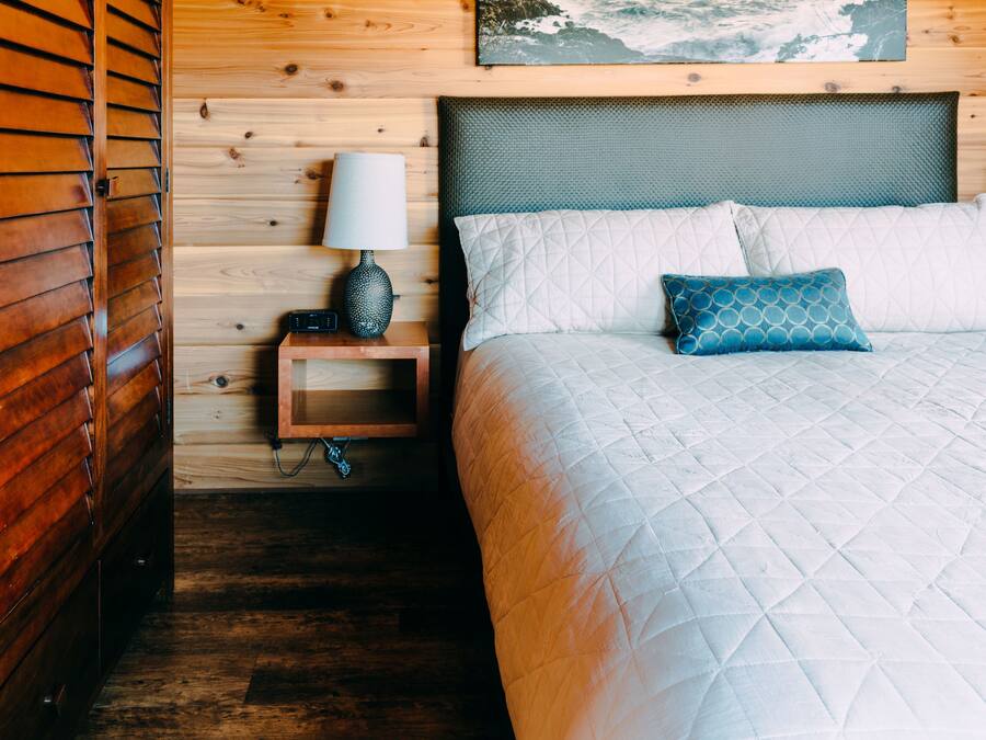 A wooden room with a bed, a nightstand, and a wall-mounted lamp.