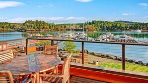 A wooden deck with a table and chairs overlooking a marina with boats and a forested hillside. - Snug Harbor Resort (Friday Harbor)