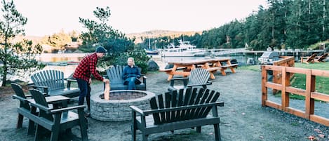Un espacio al aire libre junto al lago con sillas Adirondack, una fogata y una terraza de madera.