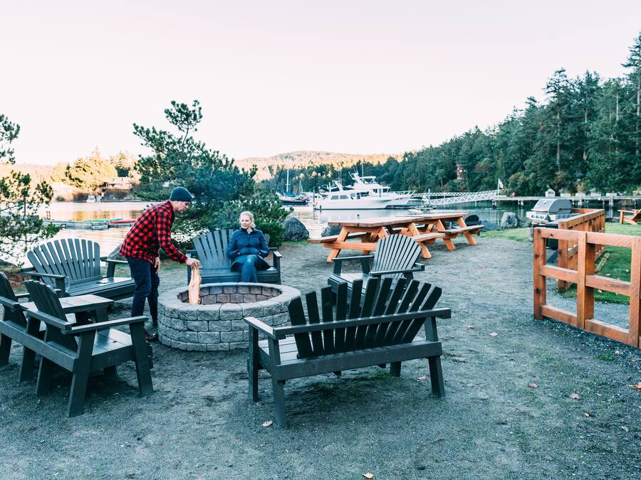 A lakeside outdoor seating area with Adirondack chairs, a fire pit, and a wooden deck.