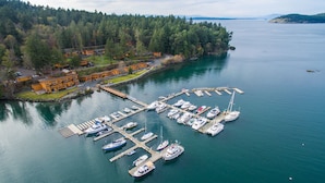 A marina with boats docked, surrounded by forested hills and a small building complex. - Snug Harbor Resort (Friday Harbor)