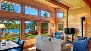 A cozy cabin interior with a large window overlooking a lake, a fireplace, and a comfortable seating area. - Snug Harbor Resort (Friday Harbor)