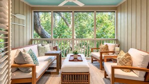 A covered porch with a ceiling fan, wooden furniture, and a view of greenery outside.