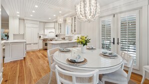 A modern kitchen with white cabinetry, a round dining table, and a unique chandelier.