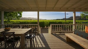 Eine überdachte Terrasse mit einem Holztisch und Stühlen, einer Bank und Blick auf einen Weinberg.