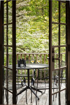 Een houten terras met metalen stoelen en een tafel, een glas wijn en verrekijkers.