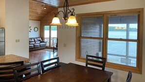 A wooden interior with a dining table, chairs, and a view of a lake through large windows. - Gorgeous New 2BR Family Beach Retreat with Paddle Boat (Sarona)
