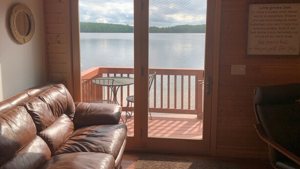 A cozy cabin room with a leather couch, a small table, and a view of a lake through a glass door. - Gorgeous New 2BR Family Beach Retreat with Paddle Boat (Sarona)