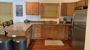 A kitchen with wooden cabinets, granite countertops, a stainless steel refrigerator, and a window with blinds. - Gorgeous New 2BR Family Beach Retreat with Paddle Boat (Sarona)