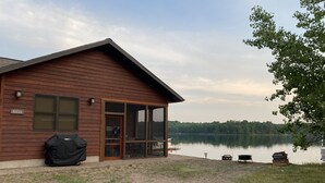 A cabin with a large sliding glass door, a covered patio, and a view of a lake. - Gorgeous New 2BR Family Beach Retreat with Paddle Boat (Sarona)