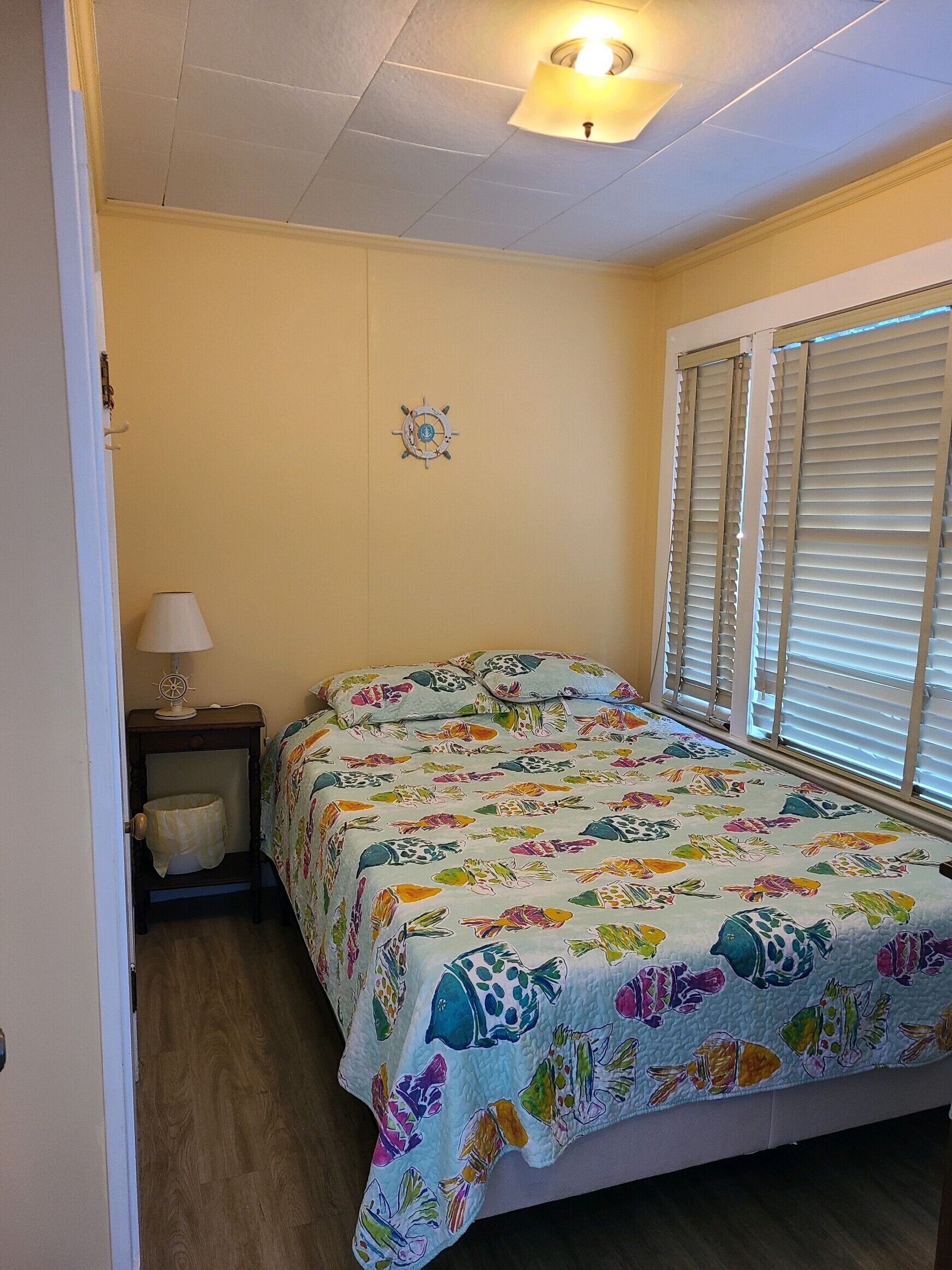 Un dormitorio con cama, mesita de noche, lámpara y ventana con persianas.
