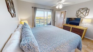 A bedroom with a bed, a TV, a dresser, and a balcony with a view.
