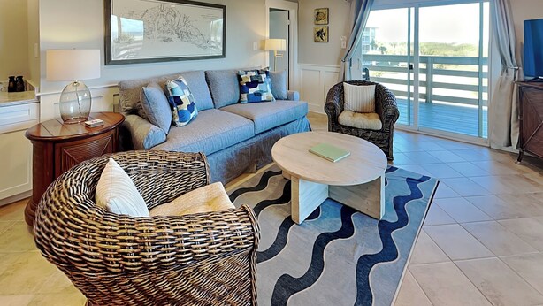 A living room with a sofa, two wicker chairs, a round coffee table, and a large window with curtains.