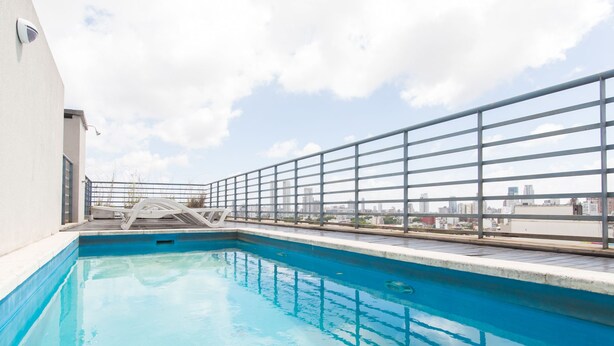 Piscina no terraço com grade de metal, vista do horizonte urbano e céu claro.