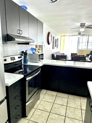A modern kitchen with a large island, black cabinets, and a stainless steel range hood.