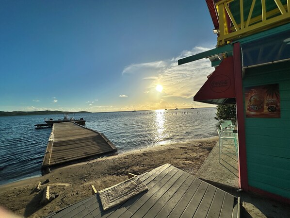 A wooden pier extending into calm waters, a clear sky, and a building with a Coca-Cola sign.