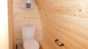 Casa de banho de uma cabana de madeira, com uma sanita, uma caixa de lenços de papel e um puxador de porta de madeira.
