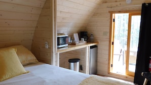 Um quarto de cabana de madeira aconchegante, com uma cama, um pequeno espaço de cozinha e uma porta que dá para uma área externa.