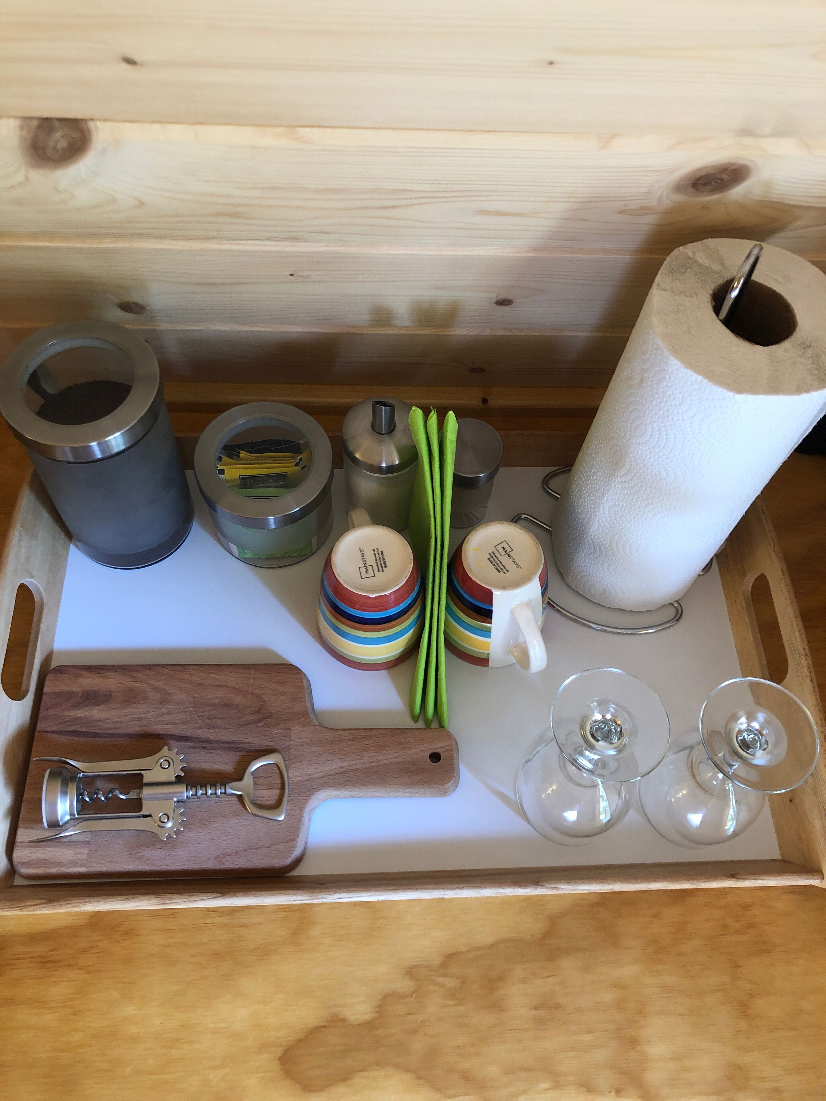 Ein Holztablett mit verschiedenen Gegenständen, darunter ein Flaschenöffner, farbenfrohe Tassen, eine Küchenrolle und grüne Bohnen.