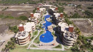Un resort con varias construcciones, una piscina central y zonas verdes circundantes.