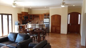 Amplia sala de estar con mesa y sillas de comedor, un sofá y una cocina con armarios de madera y un refrigerador.