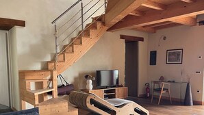 Un salon moderne avec un escalier en bois, un téléviseur et un coin repas.
