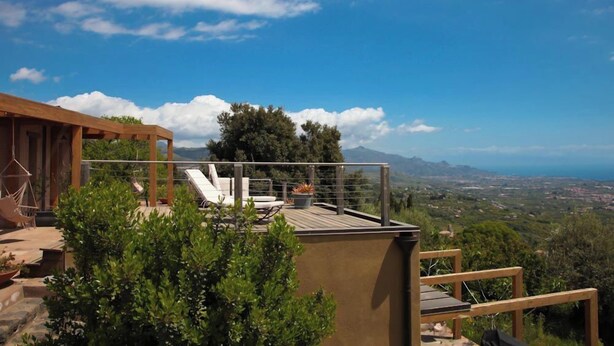 Une terrasse sur le toit, dotée de chaises longues et d’une pergola en bois, offrant une vue panoramique sur un paysage magnifique, avec des montagnes et la mer.