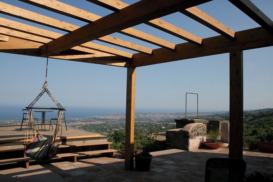 A wooden pergola with a hanging chair and a table, overlooking a cityscape.