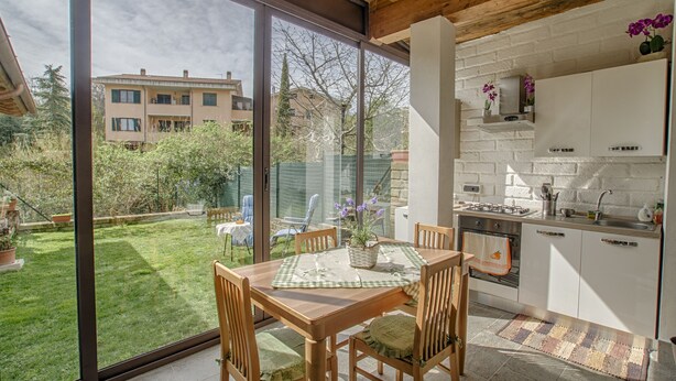 A modern kitchen with white cabinets, a built-in oven, and a large window overlooking a garden. - Independent studio in the center (bracciano)