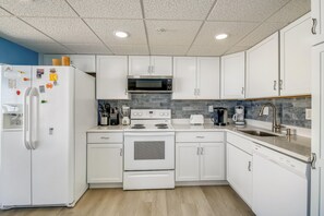 Una cocina moderna con armarios blancos, un refrigerador de acero inoxidable, un microondas integrado, una estufa y un lavamanos con grifo.