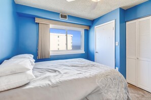 Une chambre à coucher avec un lit, une fenêtre avec des rideaux, une porte et une vue sur un bâtiment à l’extérieur.