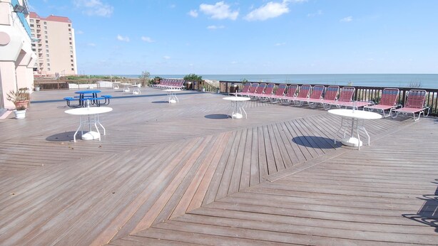 Una terraza de madera con mesas y sillas, con vista a un cuerpo de agua.