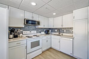 Une cuisine avec des meubles blancs, un four à micro-ondes, une cuisinière et un lave-vaisselle.