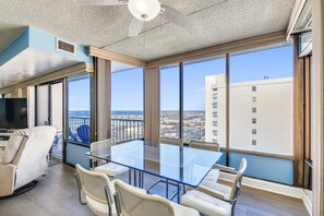 Ein geräumiger Balkon mit Glastisch und Stühlen, einem Deckenventilator und Blick auf die Stadtlandschaft.