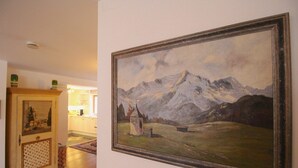 Una habitació amb un quadre gran emmarcat de paisatge de muntanya a la paret, un armari de fusta amb objectes decoratius i una catifes amb motius al sòl.