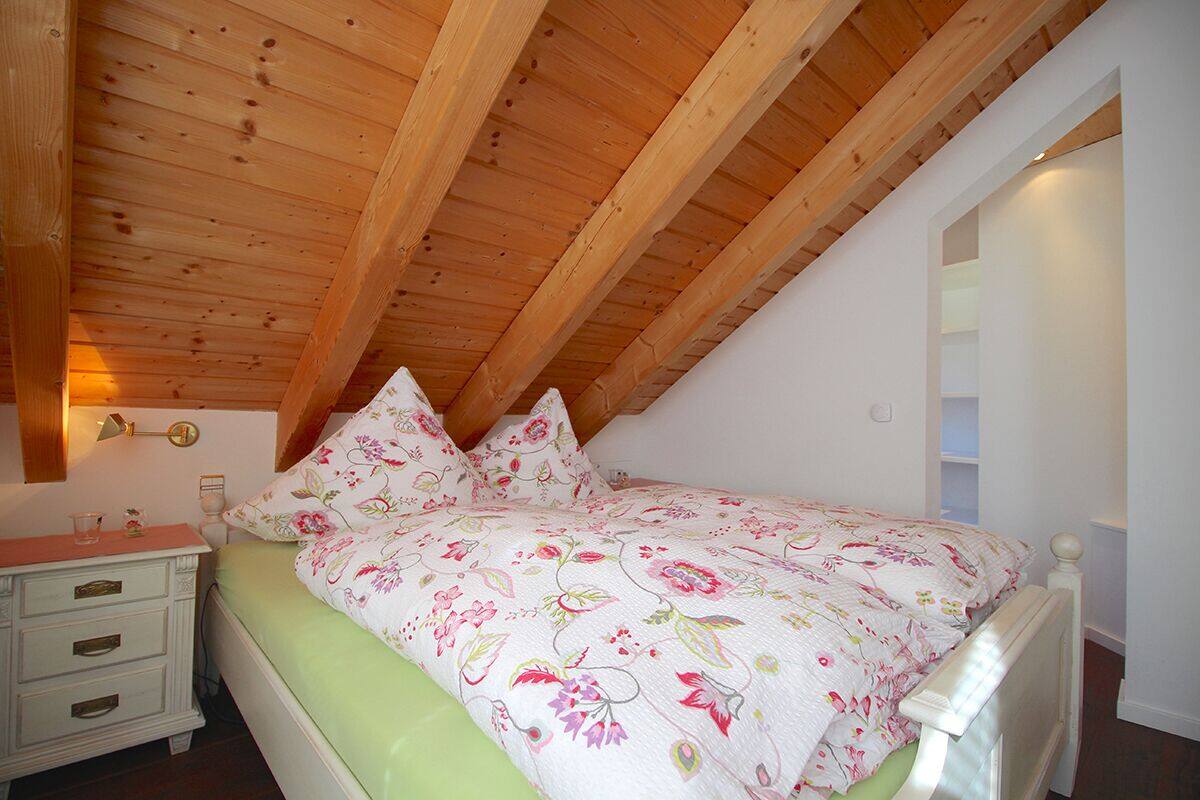 Un dormitorio con techo inclinado, una cama con ropa de cama floral, una mesita de noche y un estante de pared.