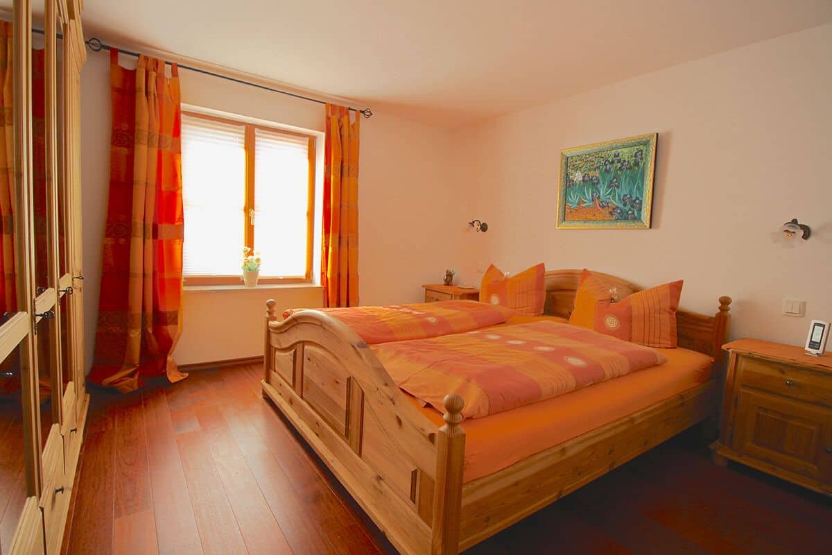 Una cama doble con cabecero de madera, una mesita de noche, cortinas en la ventana y un cuadro en la pared.