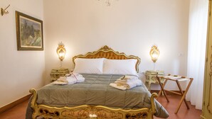A classic four-poster bed with ornate gold detailing, flanked by two bedside tables with lamps, in a room with a simple, elegant decor.