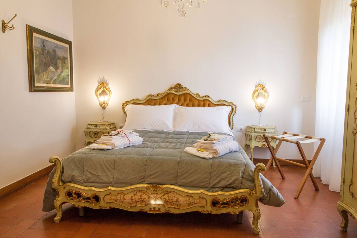 A classic four-poster bed with ornate gold detailing, flanked by two bedside tables with lamps, in a room with a simple, elegant decor.