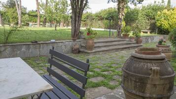 An outdoor patio with a stone wall, a wooden bench, and several potted plants.