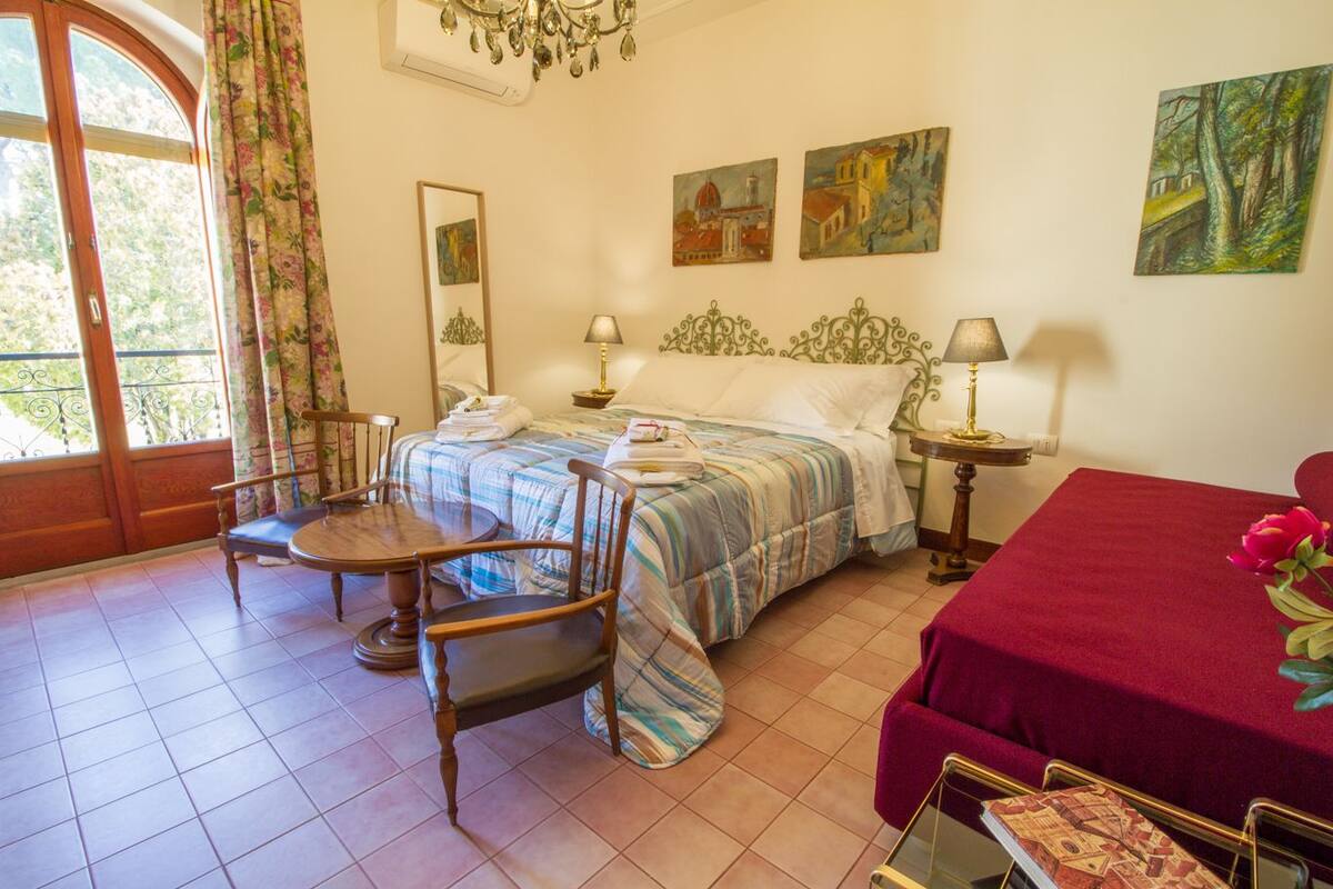A hotel room with a bed, a chair, a table, and a window with curtains.
