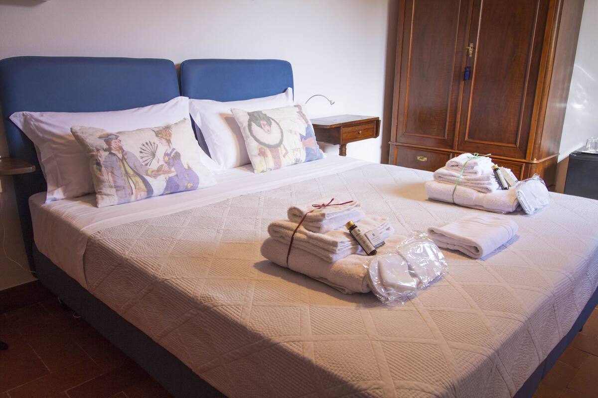 A neatly made bed with towels and toiletries, a wooden wardrobe, and a nightstand with a lamp.