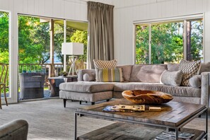Ein modernes Wohnzimmer mit einem Ecksofa, einem Couchtisch und großen Fenstern mit Blick auf Grünflächen.