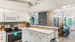 A modern kitchen with white cabinetry, a built-in oven, a stove, and a stone accent wall.