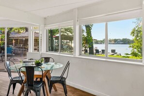 Ein Essbereich mit Glastisch und Stühlen, große Fenster mit Seeblick und Sitzgelegenheiten im Freien.