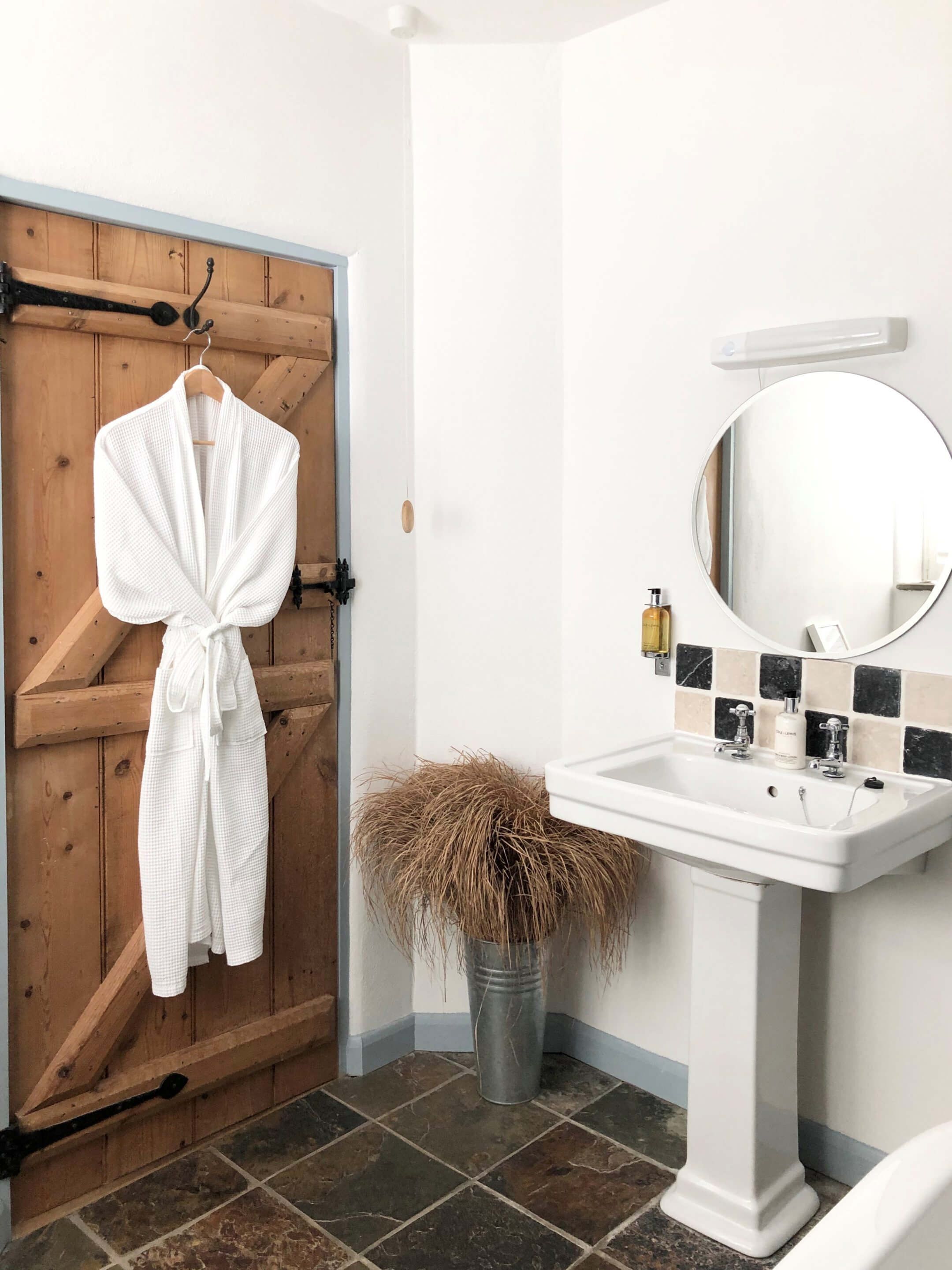 Une salle de bain avec une porte en bois, un lavabo blanc avec un miroir et une petite plante en pot.