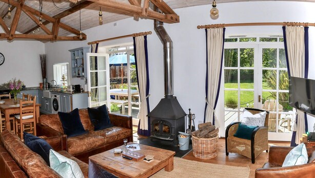 A cozy living room with a fireplace, leather sofas, a dining area, and a kitchen. - Superb detached Grade II listed barn conversion with private hot tub, close to coast (Ottery St Mary)