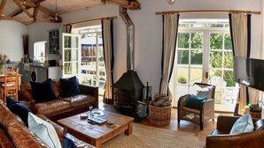 A cozy living room with a fireplace, a dining area, and a kitchen. - Superb detached Grade II listed barn conversion with private hot tub, close to coast (Ottery St Mary)
