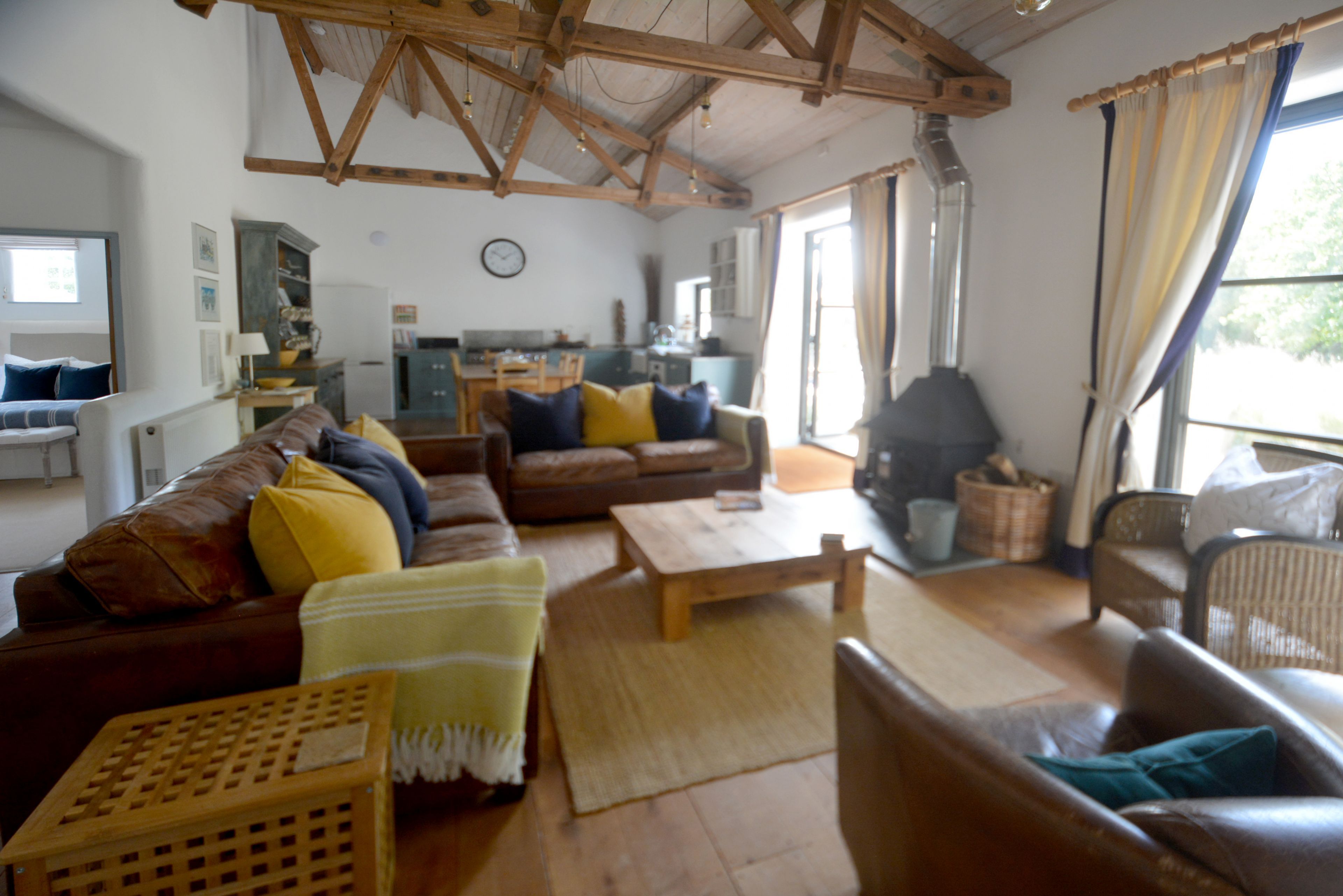 A cozy living room with a wooden ceiling, a sofa set, a coffee table, and a dining area in the background.